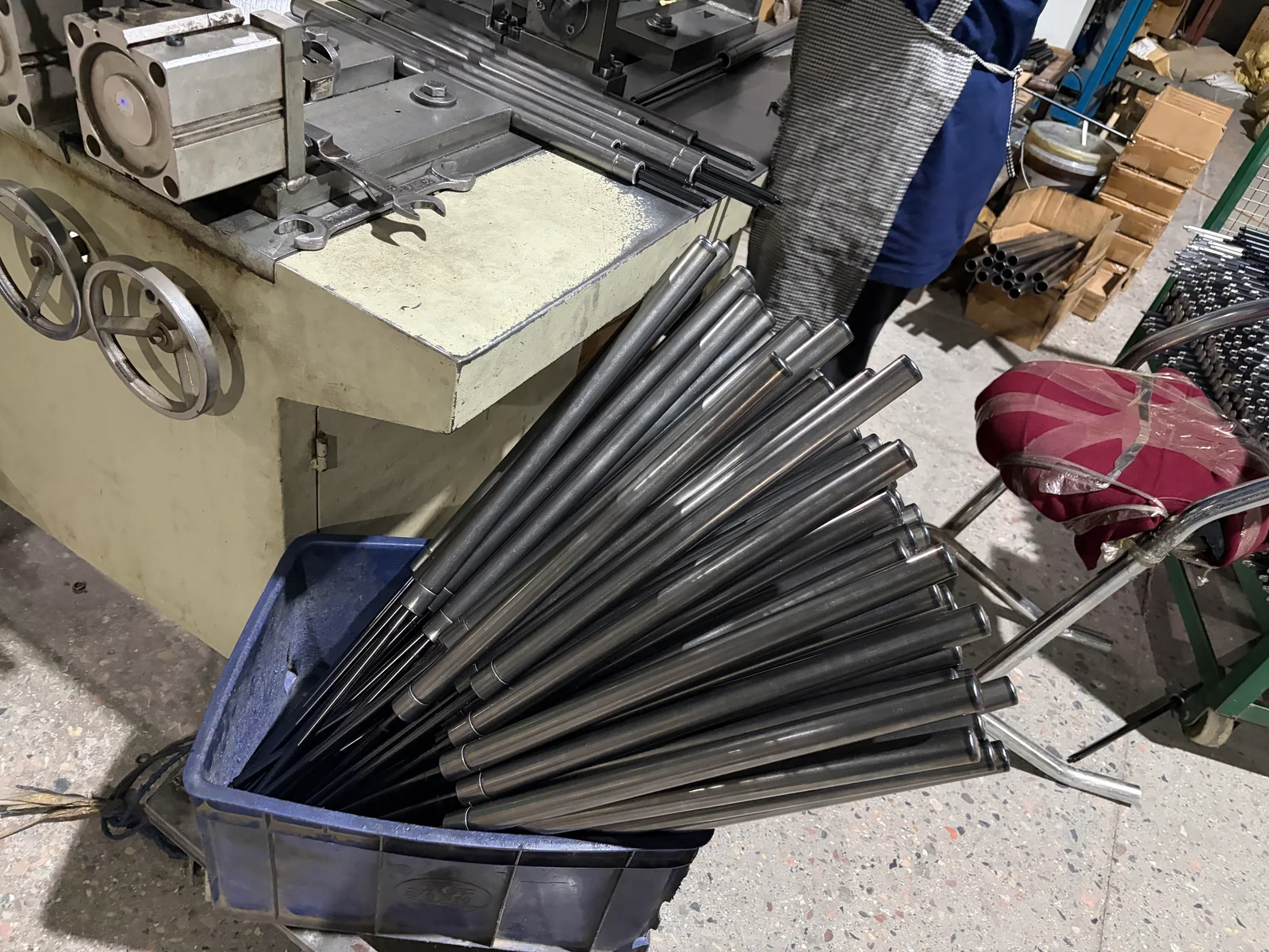 Gas spring units with silver-coloured cylinders and black rods in a blue handling bin beside a workbench